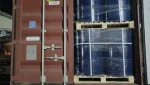 An open shipping container holds blue metal barrels stacked on wooden pallets and wrapped in plastic. The container is marked with a "Global" logo and is photographed at night.